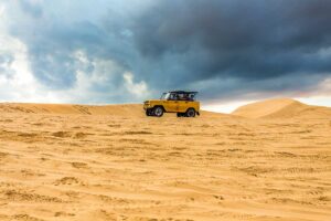 Mui Ne in July: Dark storm clouds gathering above the White Sand Dunes in Mui Ne in July, while a jeep drives across the dunes, adding a dramatic touch to the landscape.