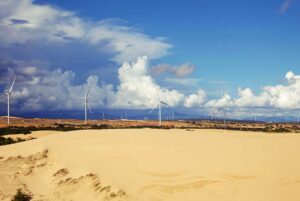 Mui Ne in September: A striking contrast at the Mui Ne Sand Dunes in September, with clear blue skies on one side and darker clouds approaching, while wind turbines stand in the distance.