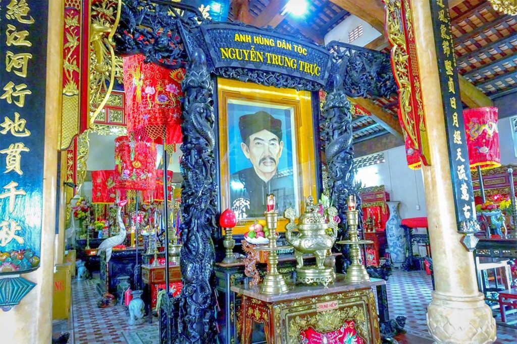 Ornate altar inside Nguyen Trung Truc Temple in Rach Gia featuring a portrait of the hero surrounded by traditional red and gold Vietnamese decorations.