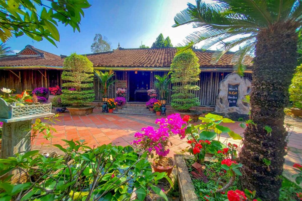Colorful garden with bonsai trees and flowers leading to the tiled courtyard and entrance of Ong Kiet’s Ancient House in Cai Be, Tien Giang, Mekong Delta.