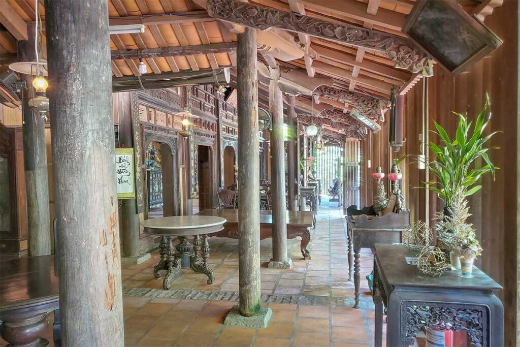 Shaded corridor with wooden beams, carved details, and tiled flooring inside Ong Kiet’s Ancient House in Cai Be, offering a glimpse of 19th-century Mekong Delta architecture.