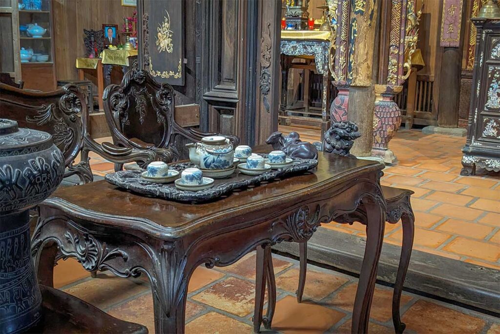 Close-up of a wooden table with a traditional ceramic tea set and carved furniture inside Ong Kiet’s Ancient House in Cai Be, reflecting the lifestyle of wealthy families in the Mekong Delta.