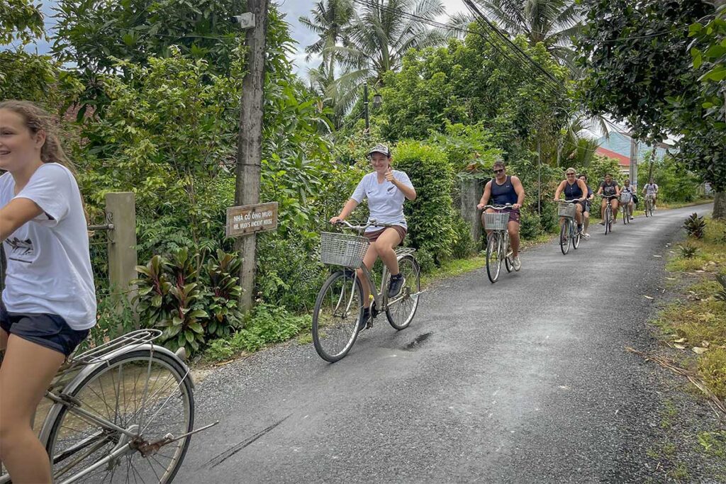 Group of travelers cycling through Cai Be countryside in Tien Giang, a popular way to combine Ong Kiet’s Ancient House visit with Mekong Delta orchard and canal scenery.