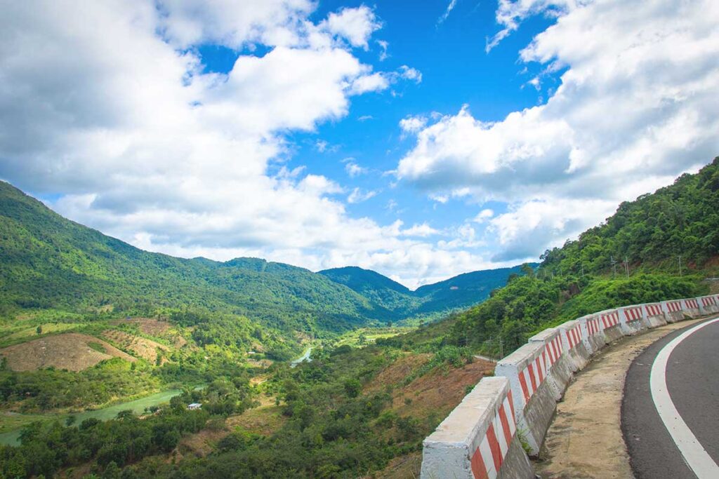 A winding section of Pha Din Pass, offering dramatic views of the surrounding mountains, hills, and a stream flowing below.