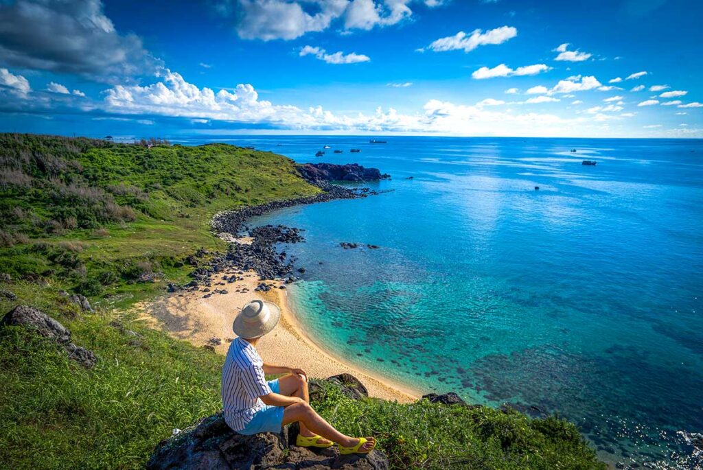 Man sitting on a hill overlooking a beach of Phu Quy Island