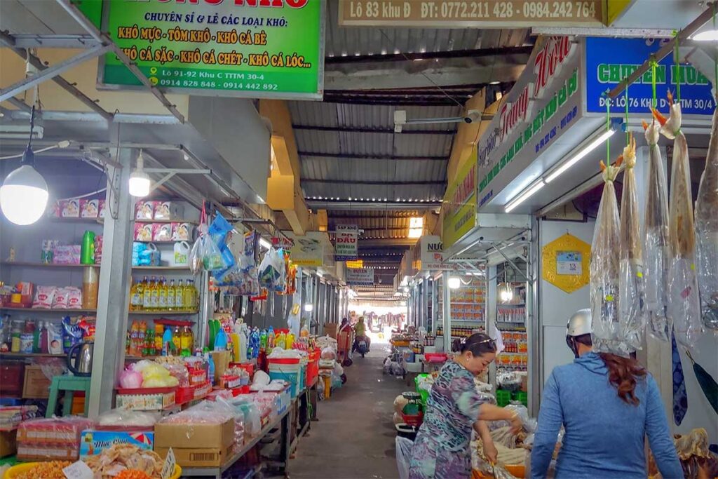 Inside Rach Gia’s central market in Vietnam, where vendors sell dried seafood, snacks, and household goods in a busy, covered shopping aisle.