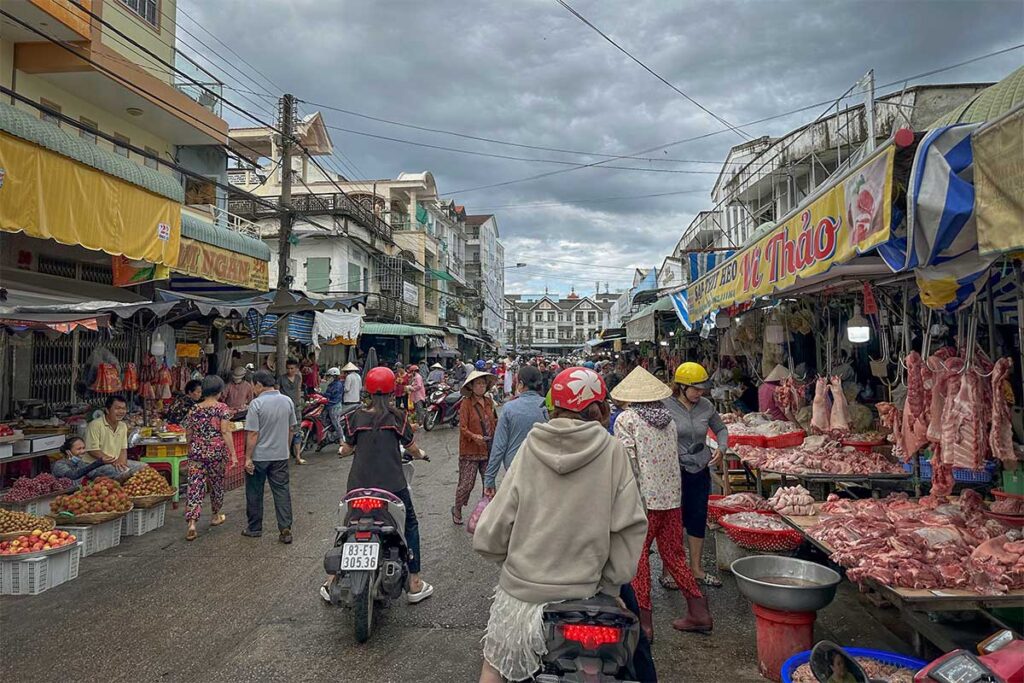 Bustling street market scene in Soc Trang with fresh meat stalls and motorbike traffic.