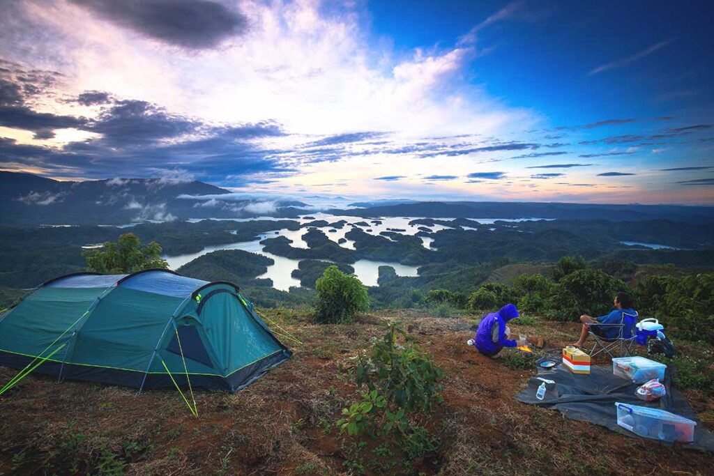 A scenic campsite on a hill with tents pitched, offering a panoramic view of Ta Dung Lake and its many islands below.