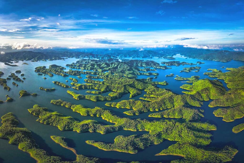 A wide aerial shot capturing the beauty of Ta Dung Lake, dotted with green islands surrounded by calm blue waters.