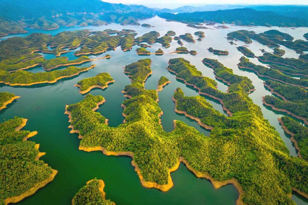 A high-altitude aerial image showcasing the vast, island-filled waters of Ta Dung Lake, nestled within the rolling hills of Dak Nong.