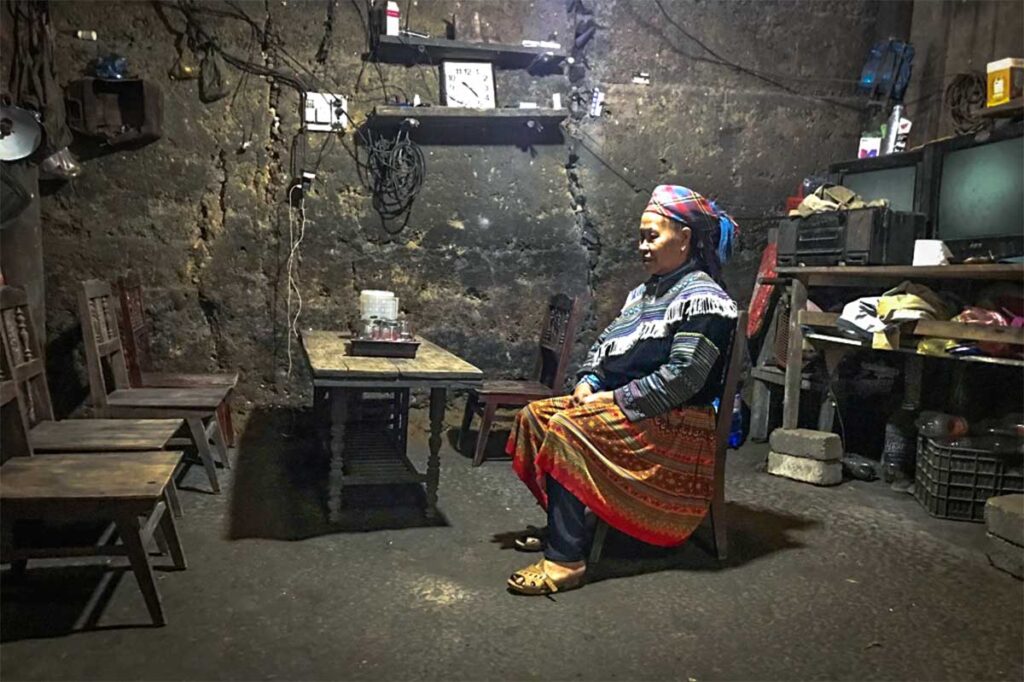 An ethnic woman traditionally dressed sitting in a dark room inside her traditional house in Ta Van Chu Village