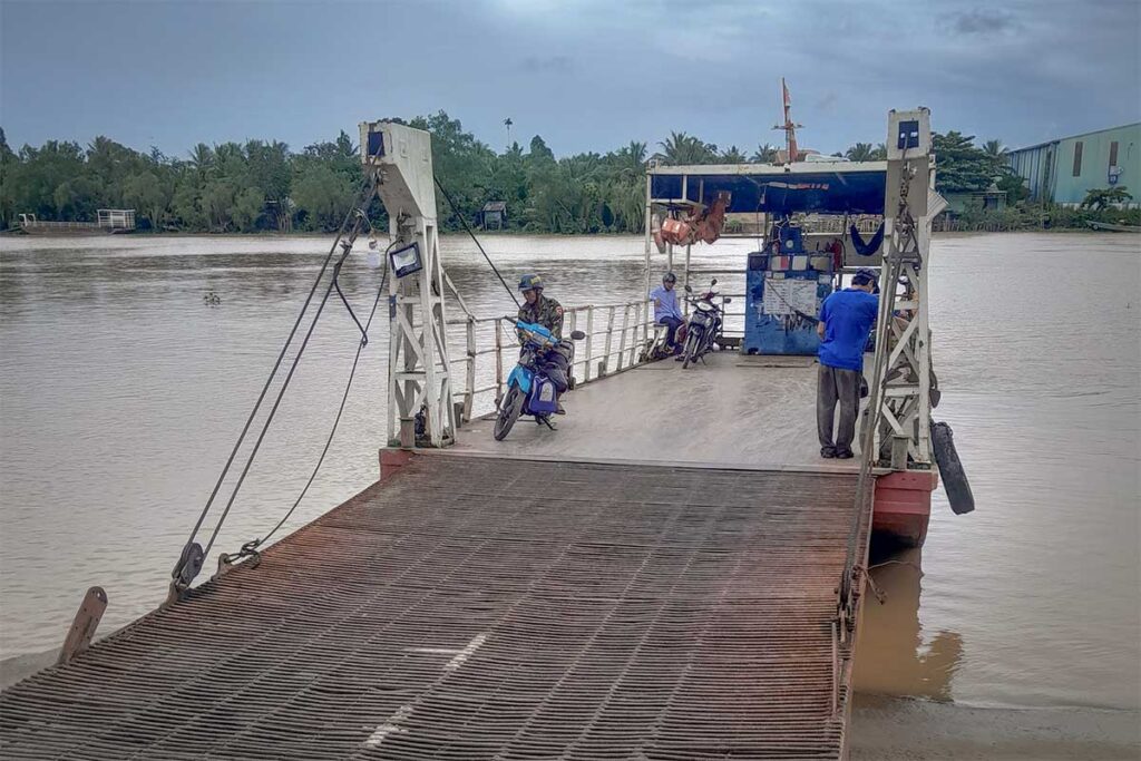 A small river ferry carries motorbikes and passengers across the Mekong Delta waters in Tra Vinh, reflecting the region’s slow-paced, practical transport.