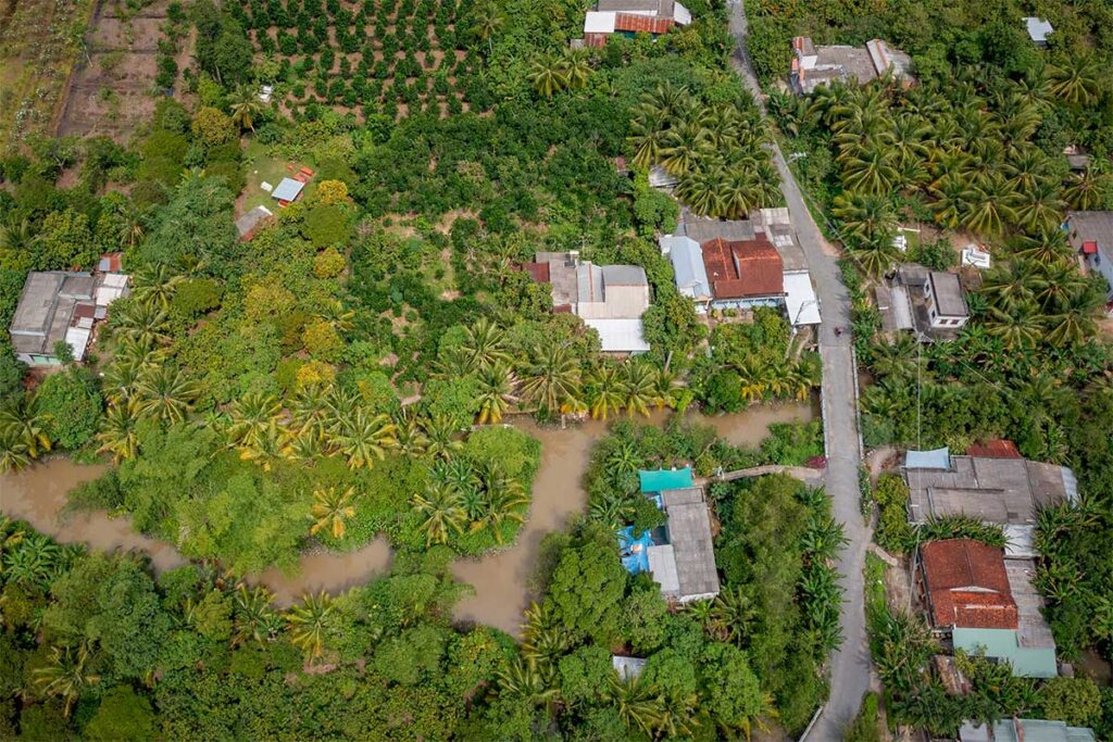 Drone photo showing lush orchards, narrow canals, and scattered houses on Tan Quy Island, a peaceful rural area in Tra Vinh, Vietnam.