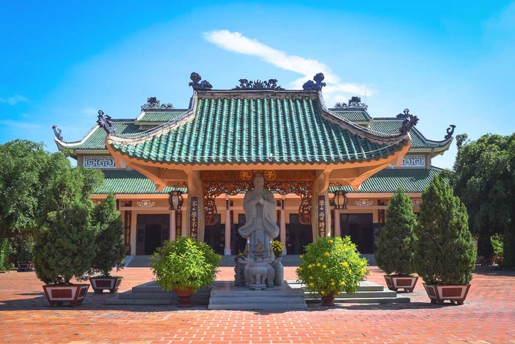 A traditional shrine in the foreground with the main temple of Tran Bien Temple of Literature in the background, showcasing its historic architecture.