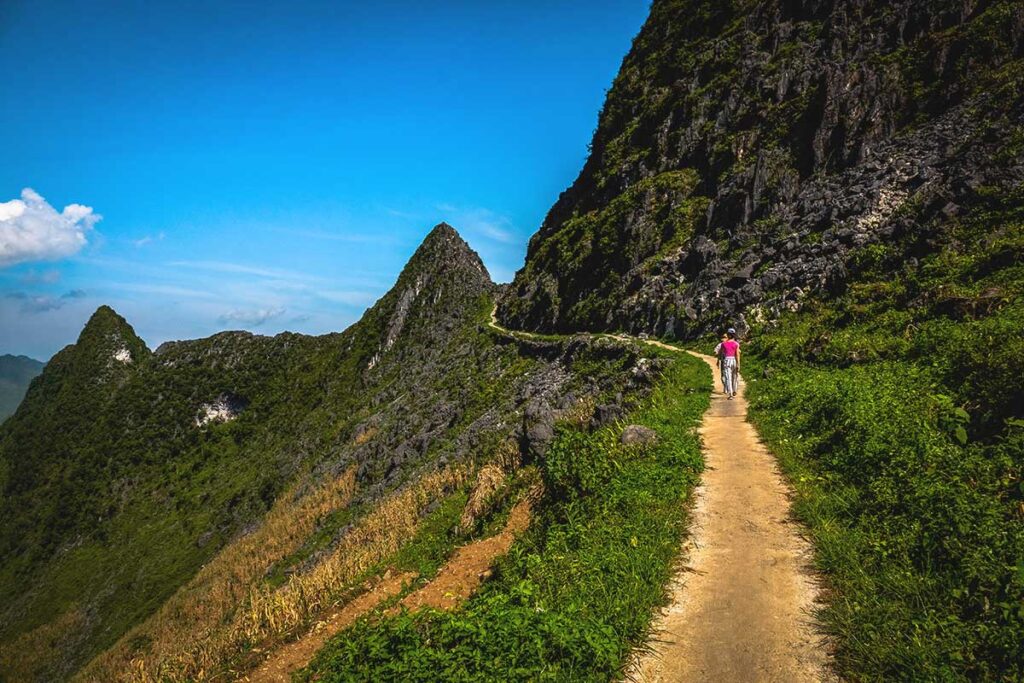 A woman walking on the Ma Pi Leng Sky Walk, a narrow mountain trail with incredible views of Ha Giang’s rugged landscape.