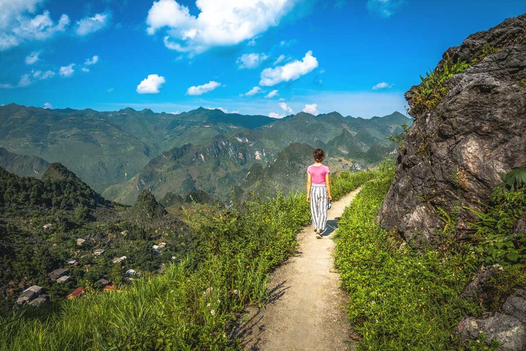 A hiker walking along a narrow path, with spectacular mountain views unfolding in the background during a trek in Ha Giang.