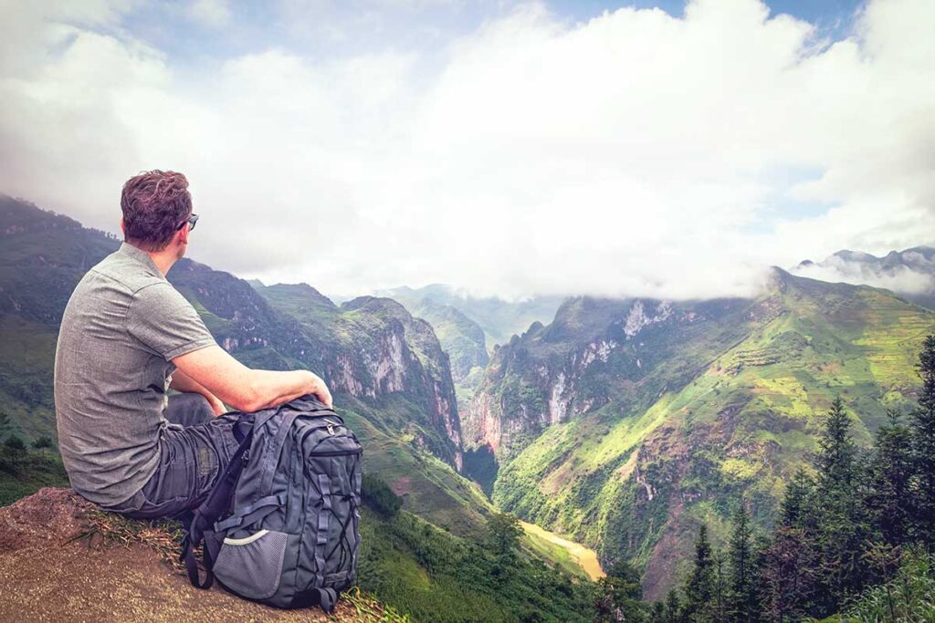 A young traveler with a backpack, sitting at a viewpoint during a trekking tour in Ha Giang, admiring the majestic landscape.