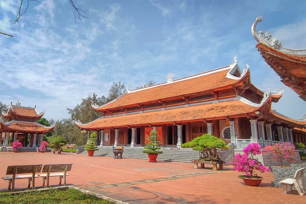 Spacious courtyard of Truc Lam Zen Monastery with traditional tiled roofs, potted plants, and red brick paving under a bright blue sky.