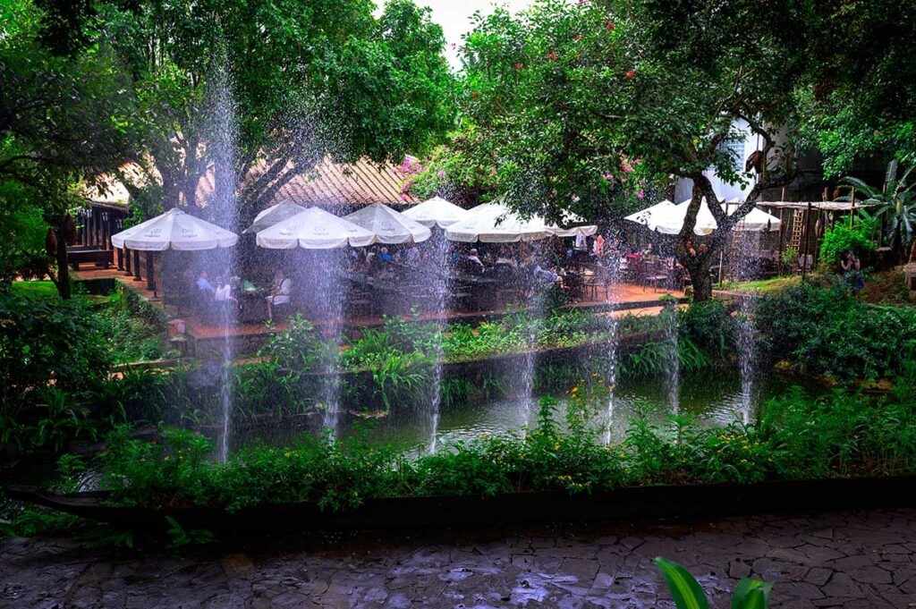 The inviting coffee shop area within Trung Nguyen Coffee Village, featuring outdoor seating amidst flowing fountains.