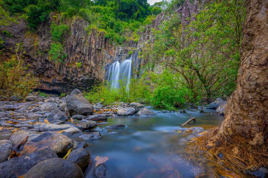 Vuc Hom Waterfall on the Van Hoa Plateau in Phu Yen, cascading from basalt cliffs into a rocky forest stream.