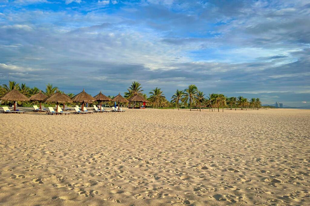 Empty stretch of golden sand at Binh Minh Beach, Vietnam, with sun loungers and palm trees creating a relaxed tropical setting.