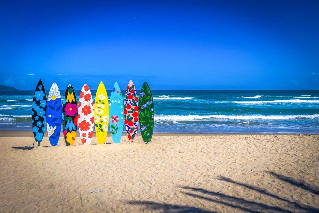 Best time to visit Da Nang – Colorful surfboards decorating the sand at My Khe Beach, with a bright blue sky and gentle waves in the background.