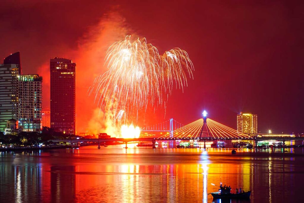 Fireworks exploding over the Han River during the Da Nang International Fireworks Festival, as seen from Dragon Bridge, with the Han River Bridge in view.