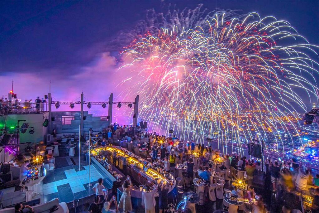 People capturing the Da Nang International Fireworks Festival from the rooftop bar Sky36, with a vibrant fireworks display lighting up the night sky.