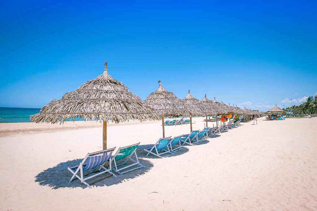 Da Nang in June – Colorful beach umbrellas and deck chairs on My Khe Beach, inviting travelers to relax under the summer sun.