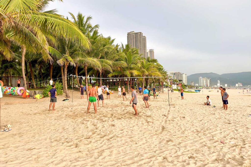 Da Nang beach in spring – A lively scene of people playing beach volleyball under pleasant weather, with golden sand and a clear blue sky.