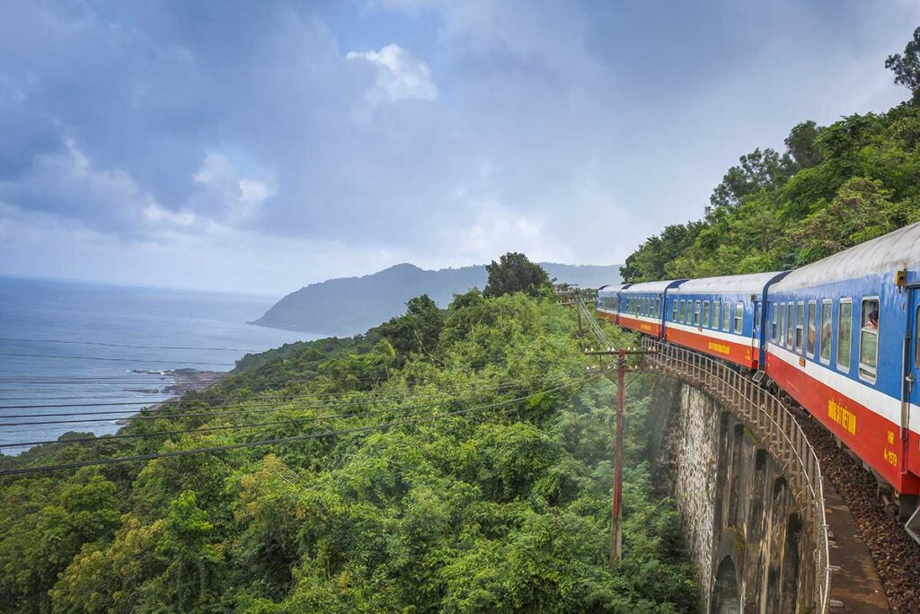 A train traveling through the Hai Van Pass on a cloudy day, with misty skies covering the mountains and coastline.