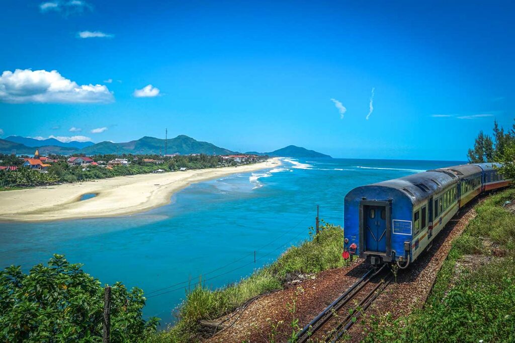 A rear view of a train traveling along the Hai Van Pass, with a stunning backdrop of Lang Co Beach and the turquoise waters below.