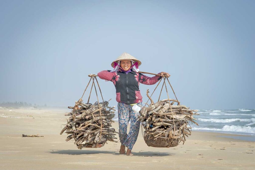 Local woman collecting driftwood on a quiet beach near Hoi An in January, when the sea can be rough and beaches are mostly empty but daily coastal life continues.