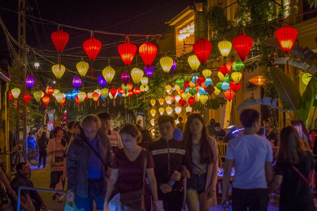Visitors walking under hanging silk lanterns during the Hoi An Lantern Festival in the Ancient Town, enjoying the lively night atmosphere.