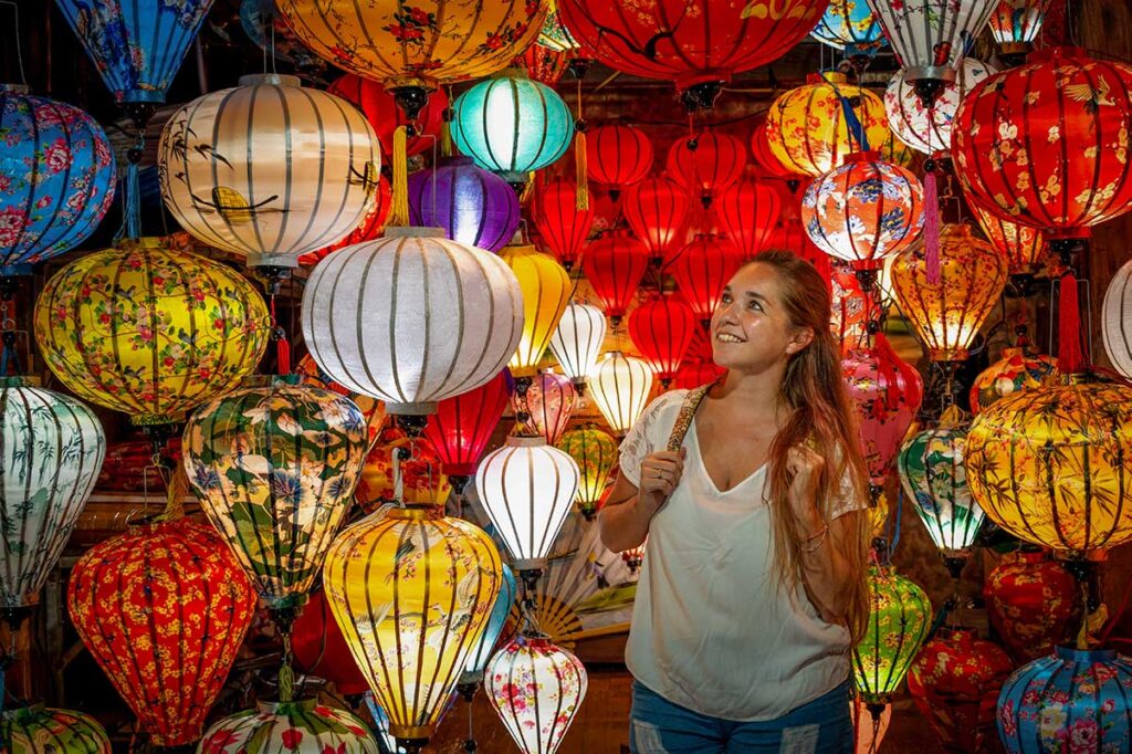 Tourist admiring handmade silk lanterns during the Hoi An Lantern Festival, surrounded by vibrant colors and traditional craftsmanship.