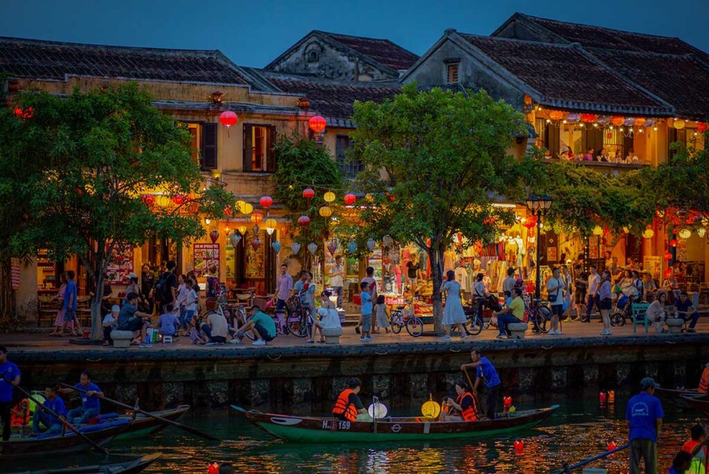 Crowds enjoying the Hoi An Lantern Festival along the riverbank, surrounded by glowing silk lanterns and ancient town architecture.