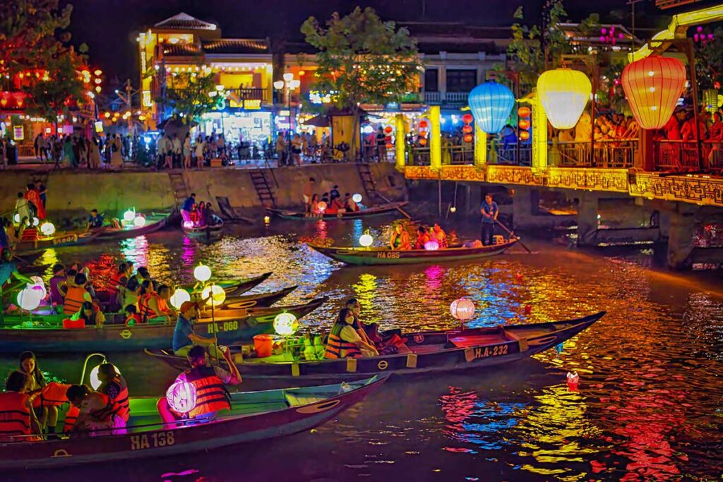 Hoi An Lantern Festival boat ride on the Thu Bon River at night, with colorful paper lanterns floating on the water and locals rowing traditional wooden boats.