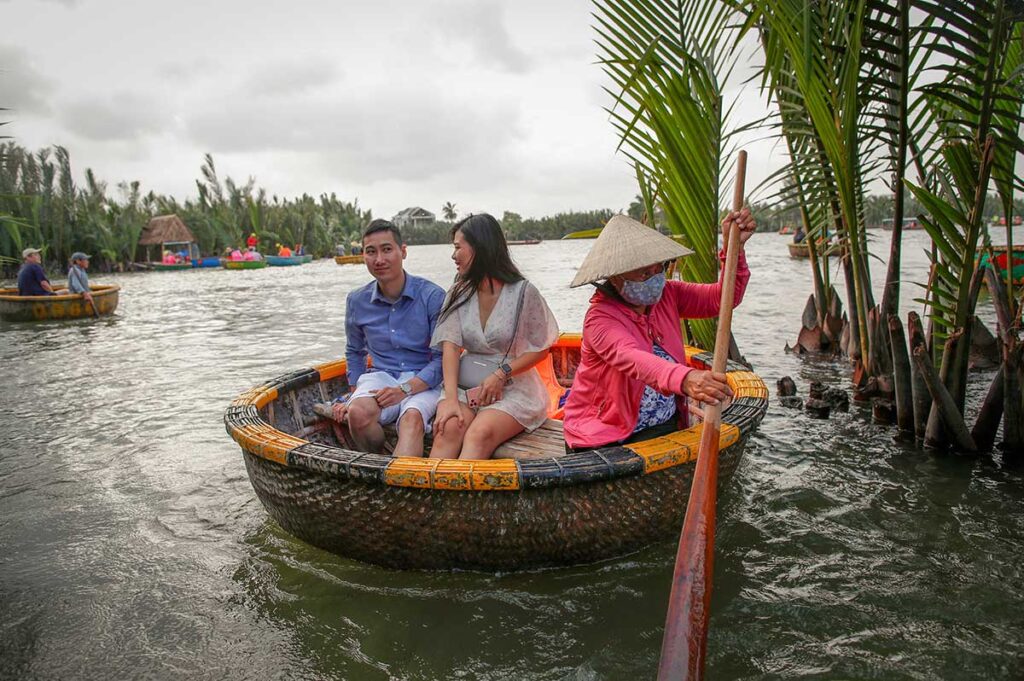 Visitors enjoying a basket boat tour through the coconut palms near Hoi An in November, as cloudy weather and light rain add to the peaceful river scenery.