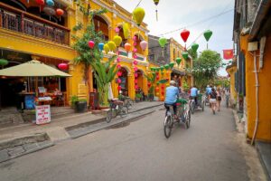 Cyclo drivers and tourists exploring Hoi An Ancient Town in October, when colorful lanterns brighten the streets despite frequent rain showers.