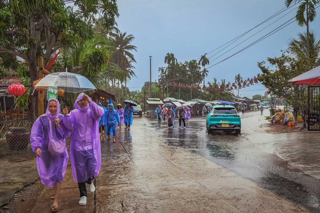 Visitors walking through Hoi An’s countryside in raincoats during a tropical downpour, a typical scene of the rainy season from October to December.