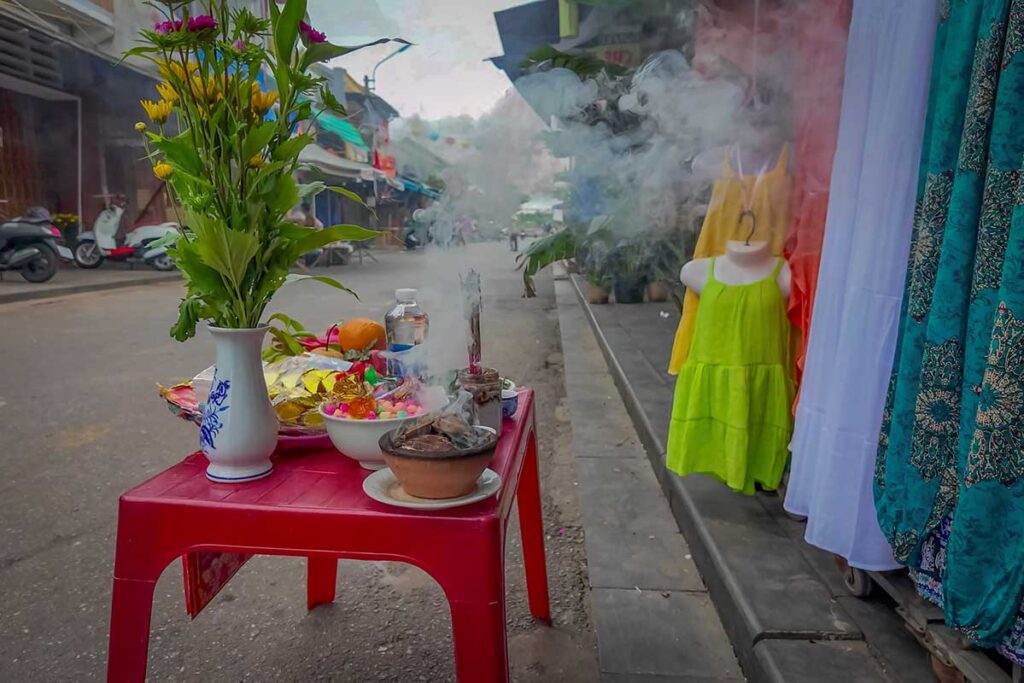 Small offering table with incense, fruit, and flowers on a Hoi An street during Tet, as locals perform traditional rituals to welcome the Lunar New Year.