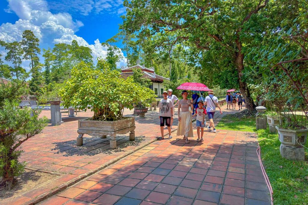 Tourists walk on a hot sunny day in Hue underneath an umbrella discovering Thien Mu Pagoda