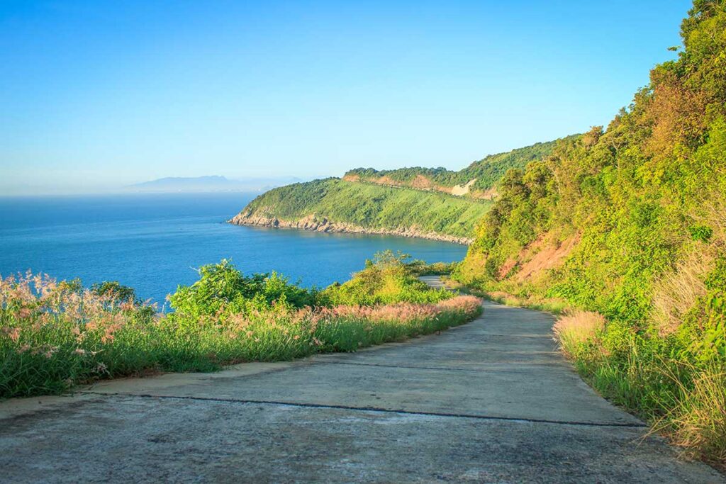 A concrete coastal road on the secluded side of Son Tra Peninsula, accessible by semi-motorbikes, offering a scenic view of the ocean.