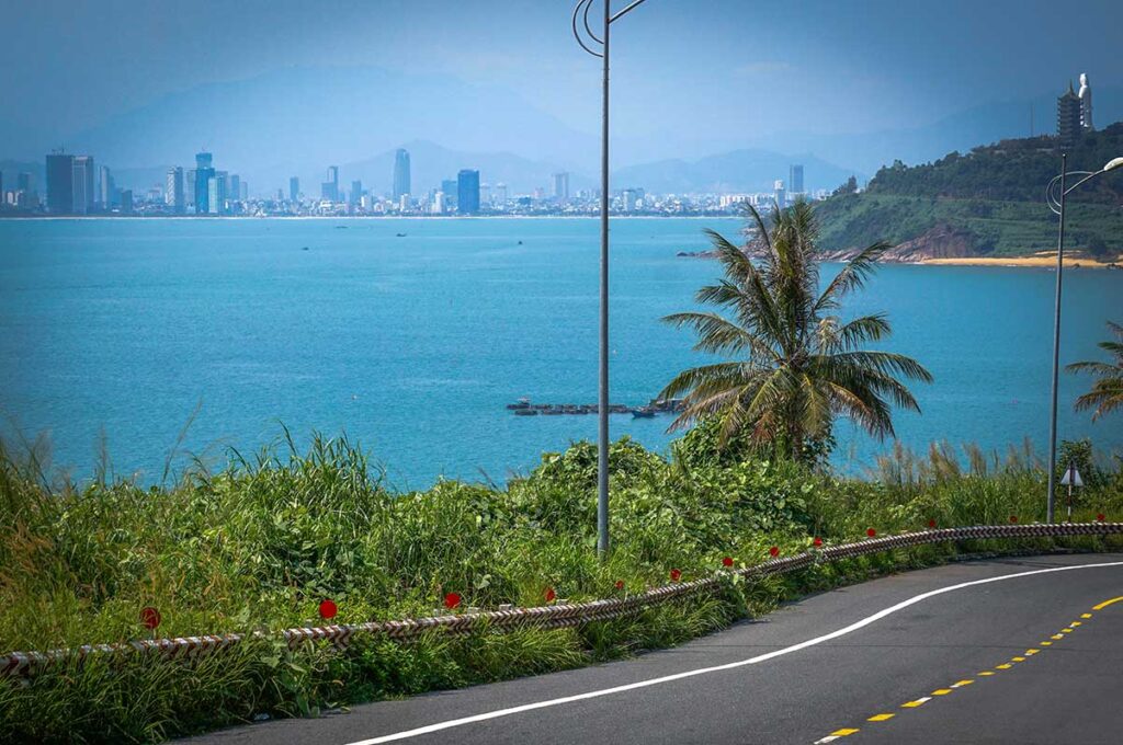 A coastal road on Son Tra Peninsula, with the ocean on one side and Da Nang City's skyline visible in the background.