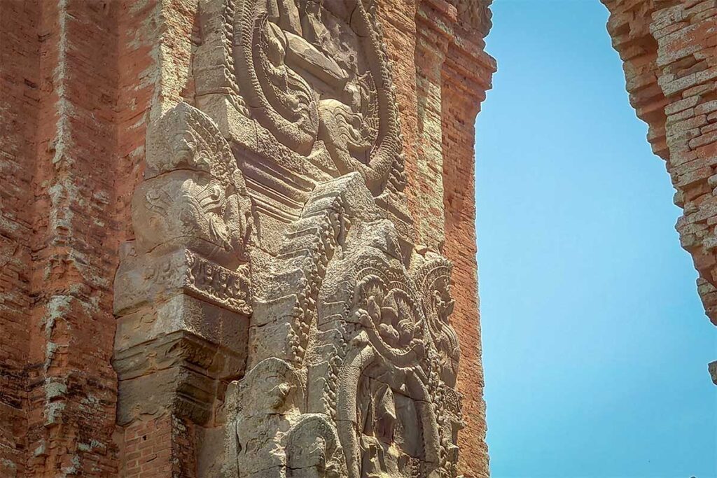 Cham tower facade carvings in Quy Nhon – Intricate stone reliefs and Hindu motifs on the red brick wall of the Twin Towers under a bright sky.