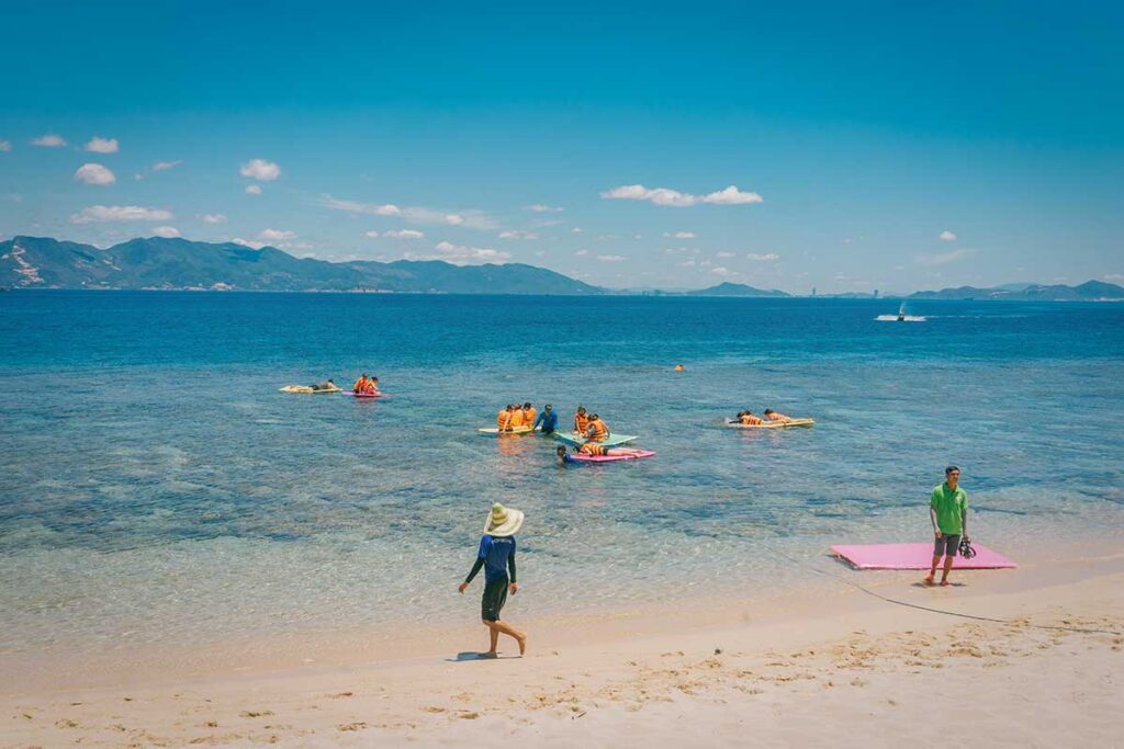 Tourists with lifejackets snorkeling and floating near shallow reef at Cu Lao Xanh beach.
