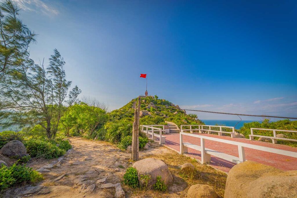 Youth flagpole on Cu Lao Xanh Island, a national sovereignty marker with sea views and a stone path leading up the hill.