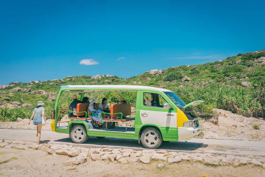 Electric sightseeing cart used for getting around Cu Lao Xanh Island, driving on a small paved road through rocky scenery.
