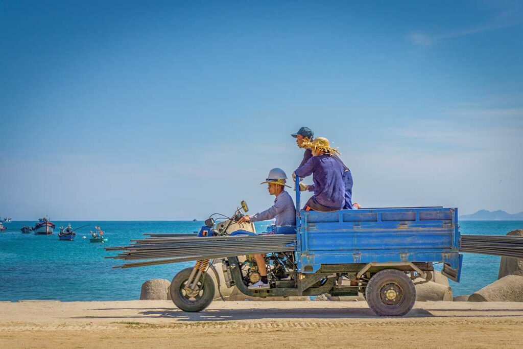 Local fishermen transporting goods on a three-wheeled motorbike in Cu Lao Xanh village, reflecting daily island life.