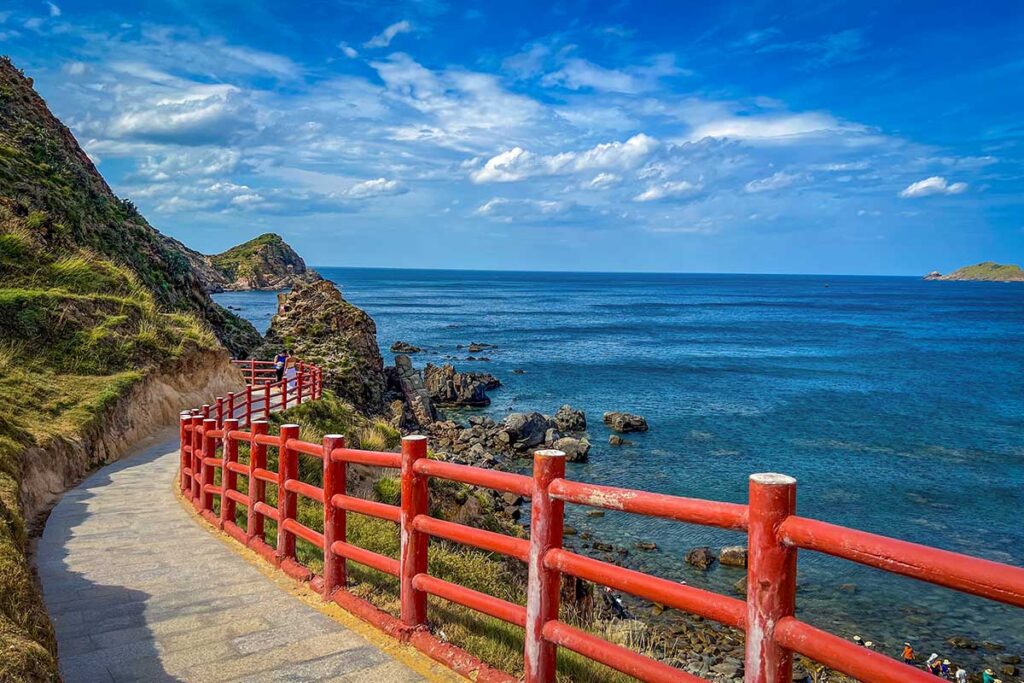 Curved walkway with red railings overlooking the blue sea along the cliffs at Eo Gió
